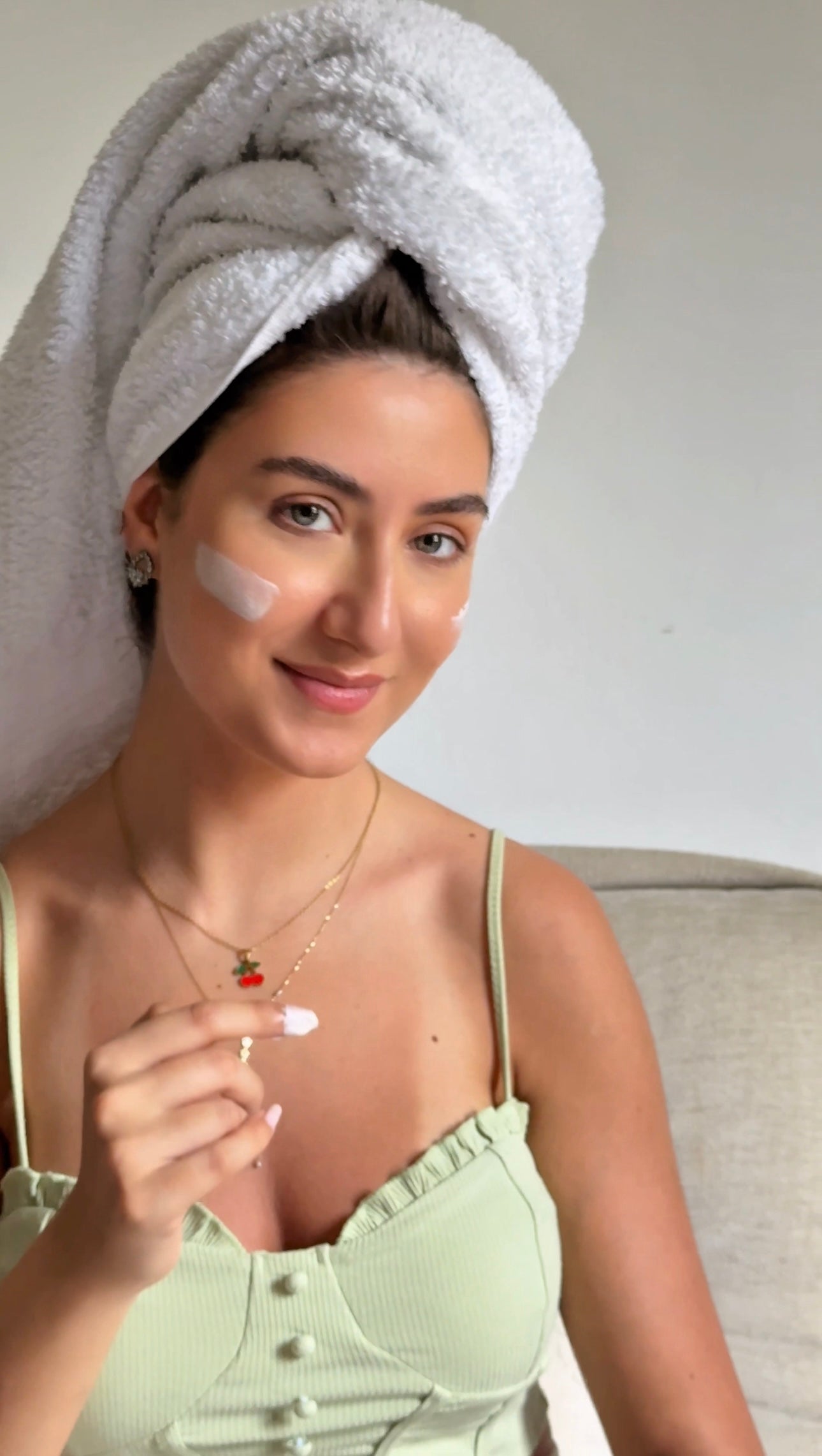 Woman with a towel wrapped around her head, applying cream to her face.